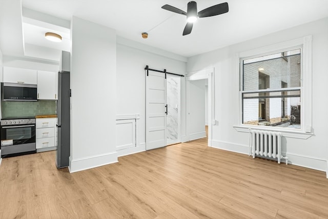 interior space with a barn door, radiator, stainless steel fridge, and light hardwood / wood-style flooring