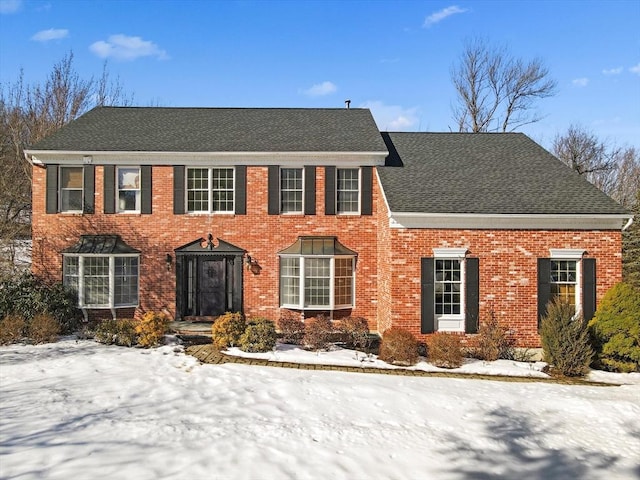 colonial home featuring brick siding and roof with shingles