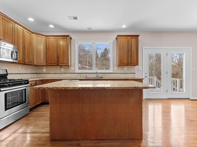 kitchen with a sink, a kitchen island, light wood-style floors, appliances with stainless steel finishes, and light stone countertops