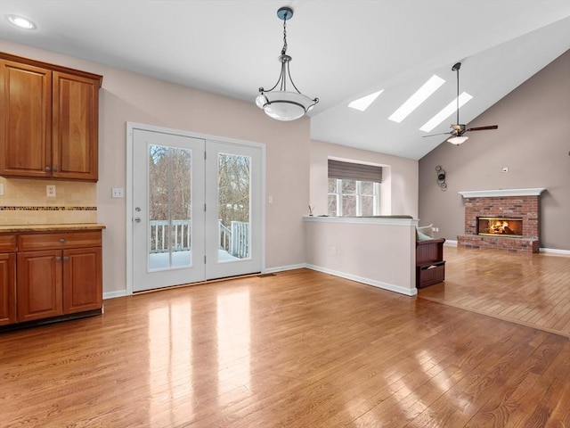 interior space with light wood-style floors, lofted ceiling with skylight, a brick fireplace, ceiling fan, and baseboards