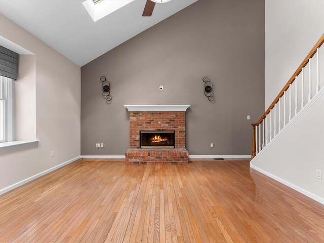 unfurnished living room with high vaulted ceiling, baseboards, stairway, a brick fireplace, and light wood finished floors