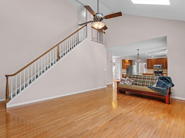 living area featuring a skylight, baseboards, ceiling fan, stairs, and light wood-type flooring