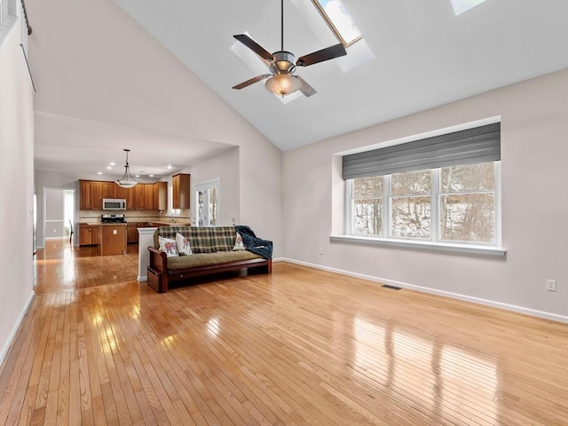 living room with a skylight, visible vents, light wood-style flooring, and baseboards