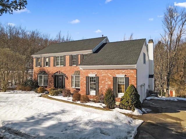 view of front facade with brick siding, a chimney, a shingled roof, a garage, and driveway