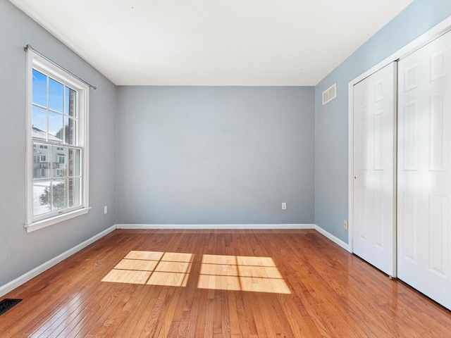 unfurnished bedroom with hardwood / wood-style flooring, a closet, visible vents, and baseboards