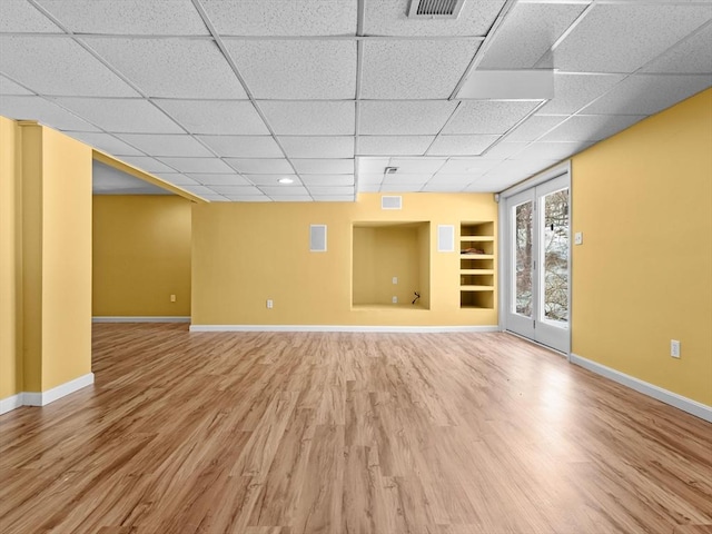 spare room with a paneled ceiling, wood finished floors, visible vents, built in features, and baseboards