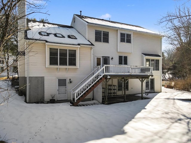 snow covered house with a deck, a chimney, and stairway