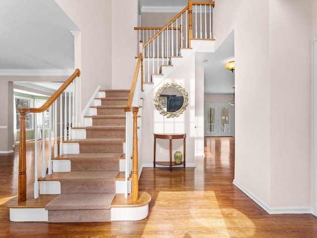 stairs with crown molding, wood finished floors, a towering ceiling, and baseboards