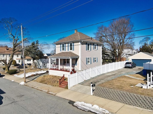 american foursquare style home with a fenced front yard, roof with shingles, a detached garage, covered porch, and a residential view