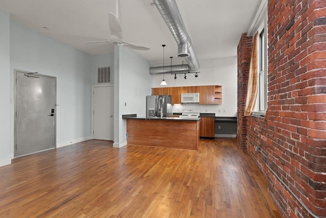 kitchen with a towering ceiling, white appliances, dark countertops, and wood finished floors