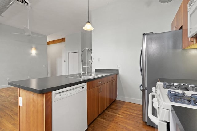 kitchen with a peninsula, white appliances, dark countertops, and a sink