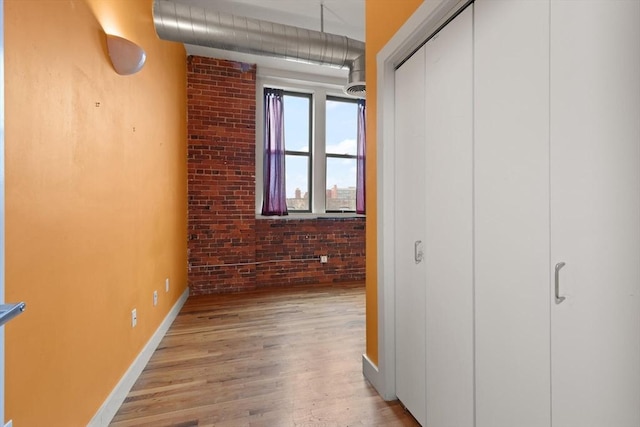 unfurnished bedroom featuring light wood-style floors, a closet, baseboards, and brick wall