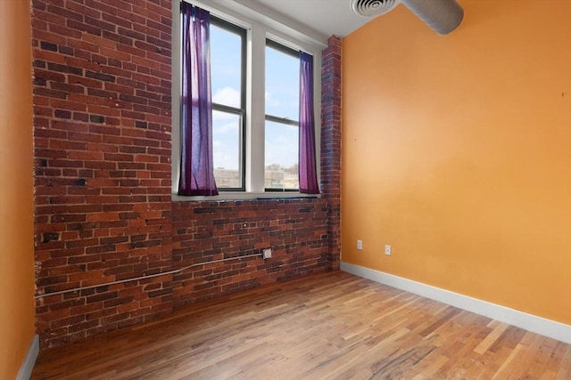 empty room featuring brick wall, baseboards, visible vents, and light wood finished floors