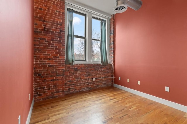 empty room with light wood-style floors, brick wall, visible vents, and baseboards