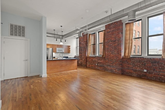 unfurnished living room with brick wall, light wood-type flooring, and visible vents