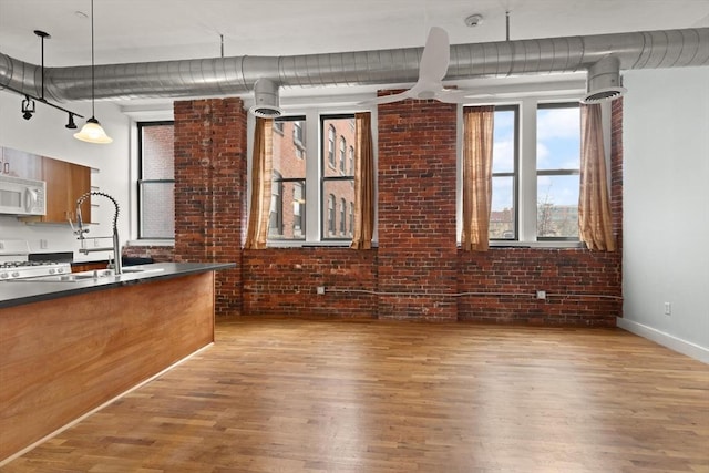 interior space featuring brick wall, white appliances, a sink, light wood-style floors, and dark countertops