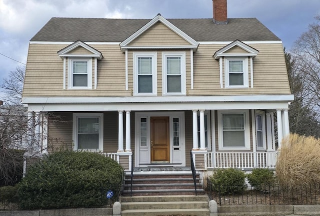 view of front of property featuring covered porch, roof with shingles, and a chimney