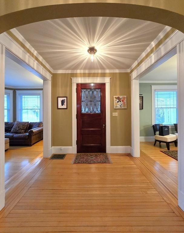 foyer entrance featuring ornamental molding, arched walkways, light wood-type flooring, and plenty of natural light