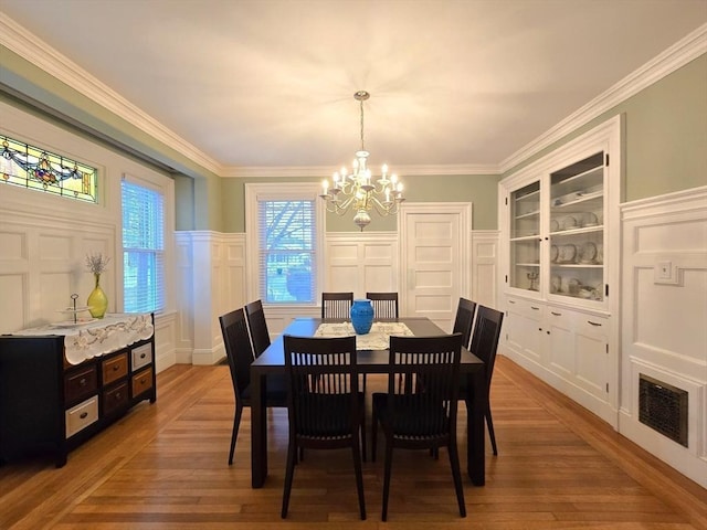 dining space featuring built in shelves, a notable chandelier, a decorative wall, visible vents, and crown molding