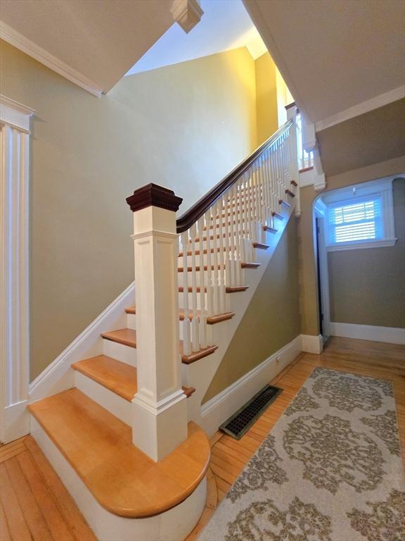 stairway featuring crown molding, wood finished floors, visible vents, and baseboards