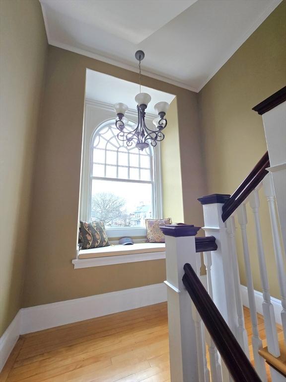 stairs with baseboards, crown molding, wood finished floors, and an inviting chandelier