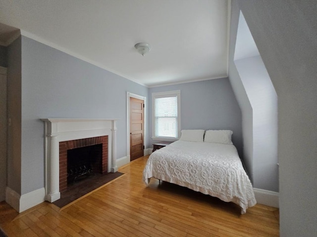 bedroom with a brick fireplace, wood finished floors, and baseboards