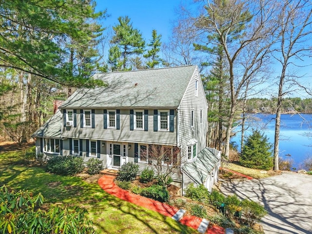 view of front of property with a shingled roof, a chimney, a front lawn, and a water view
