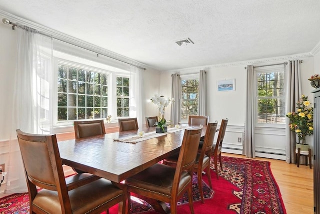 dining space featuring light wood finished floors, a textured ceiling, visible vents, ornamental molding, and a baseboard radiator