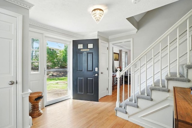 entryway with stairway, crown molding, a notable chandelier, and light wood finished floors