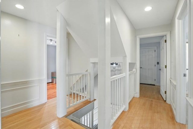 hallway with recessed lighting, light wood-style floors, a wainscoted wall, and an upstairs landing