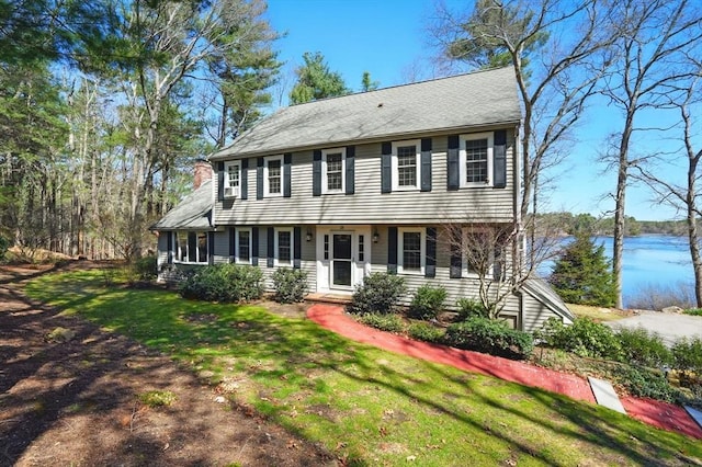 colonial home featuring a chimney, a water view, and a front yard
