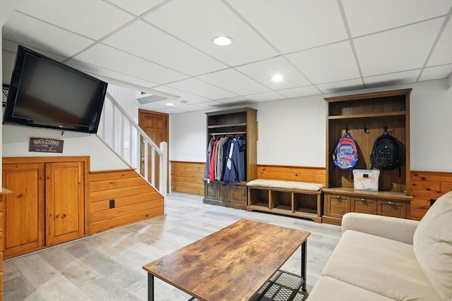 living area with light wood-style floors, a drop ceiling, wood walls, and wainscoting