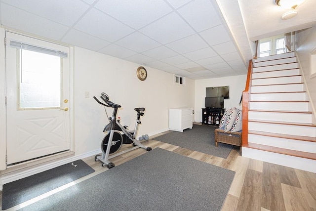 exercise area featuring wood finished floors, a drop ceiling, visible vents, and baseboards