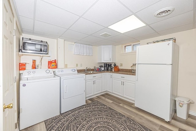 laundry area with laundry area, washing machine and clothes dryer, light wood finished floors, a sink, and visible vents