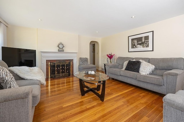 living area featuring a brick fireplace, light wood finished floors, arched walkways, and recessed lighting