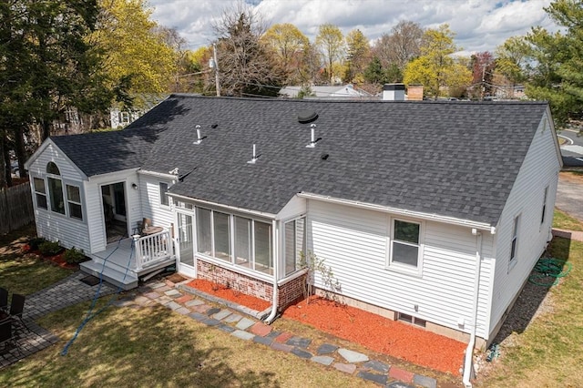 rear view of house with a wooden deck, a shingled roof, a sunroom, and a lawn