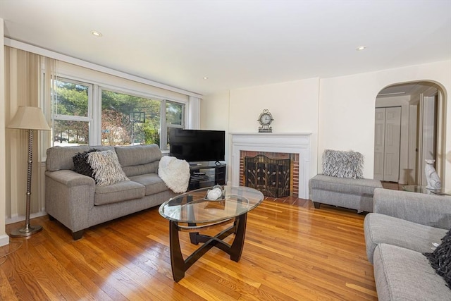 living area featuring a brick fireplace, arched walkways, and light wood-style flooring