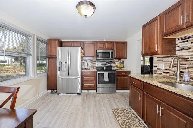 kitchen with tasteful backsplash, appliances with stainless steel finishes, light wood finished floors, and a sink