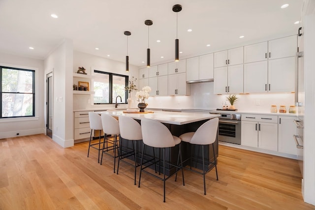 kitchen featuring light hardwood / wood-style floors, oven, white cabinetry, and pendant lighting