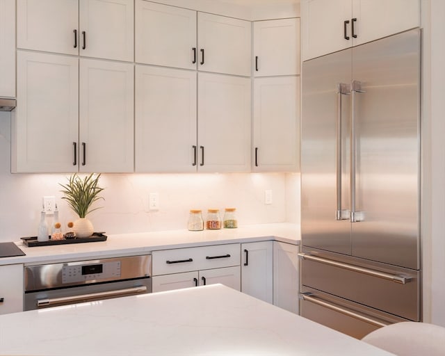 kitchen featuring stainless steel appliances, white cabinets, light stone counters, and decorative backsplash