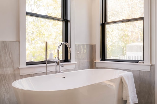 bathroom with plenty of natural light, a bathing tub, and tile walls