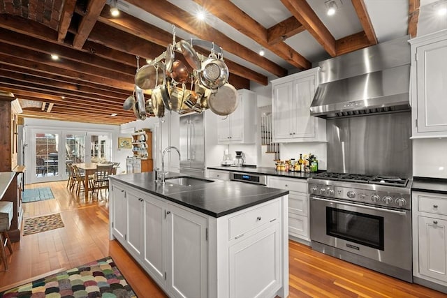 kitchen featuring stainless steel stove, a sink, wall chimney range hood, dark countertops, and light wood-type flooring