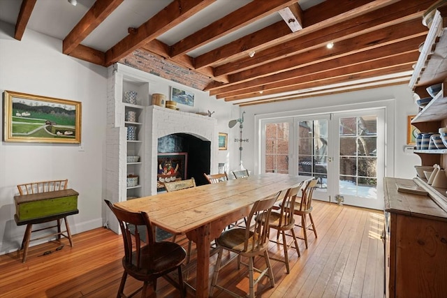 dining area with beamed ceiling, light wood finished floors, and a brick fireplace