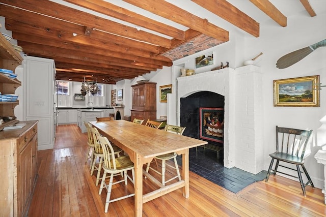 dining space with beam ceiling, light wood finished floors, a fireplace, and a chandelier