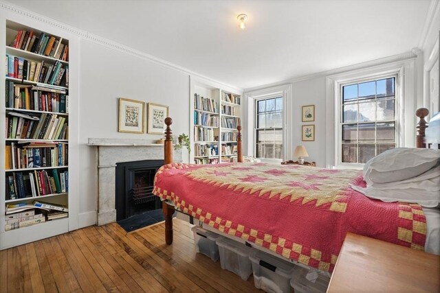 bedroom with hardwood / wood-style flooring, a fireplace with flush hearth, and crown molding