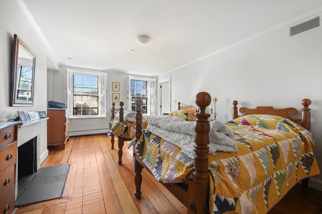 bedroom featuring a baseboard heating unit, light wood finished floors, and ornamental molding