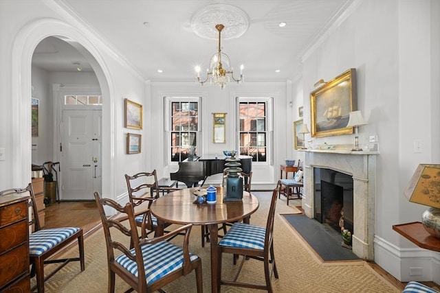 dining area with arched walkways, a chandelier, crown molding, a high end fireplace, and recessed lighting