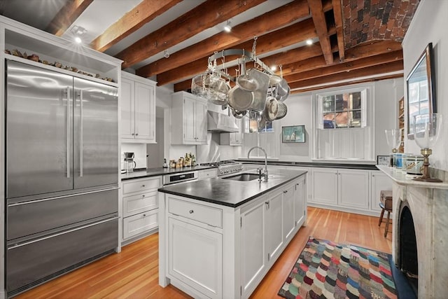 kitchen featuring stainless steel built in refrigerator, a sink, dark countertops, light wood-style flooring, and white cabinets