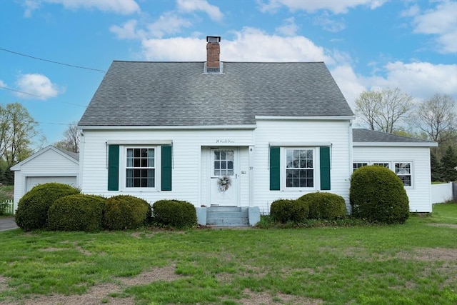 cape cod house with a chimney, roof with shingles, a front yard, and a garage