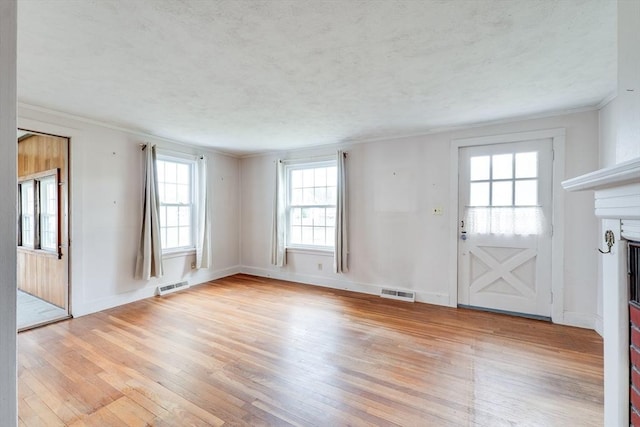 unfurnished living room with light wood finished floors, healthy amount of natural light, ornamental molding, baseboards, and a textured ceiling